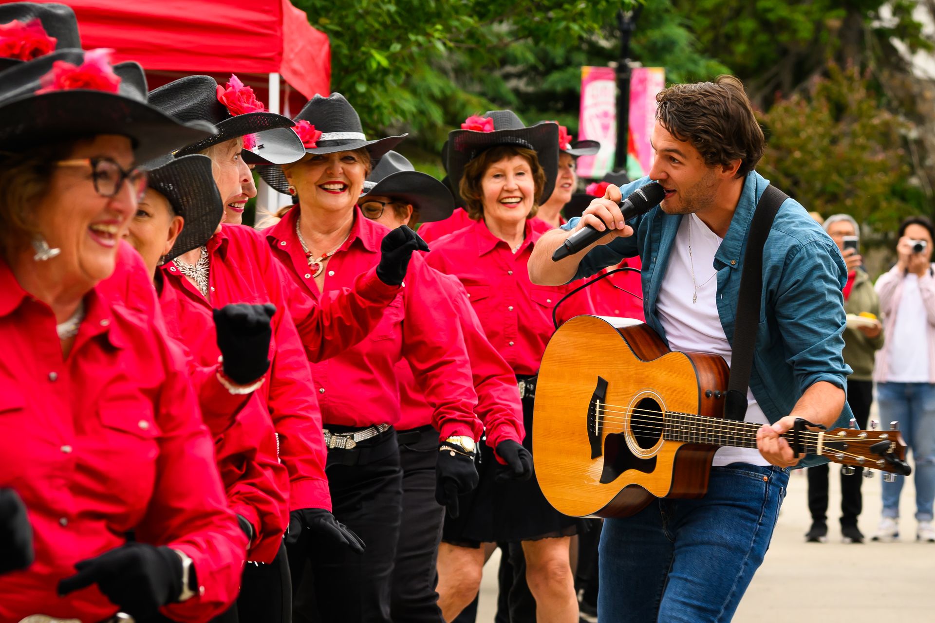 Women dancers in cowboy hats at a gathering in Calgary, Alberta celebrating the Calgary Stampede. Male singer walks through the crowd.