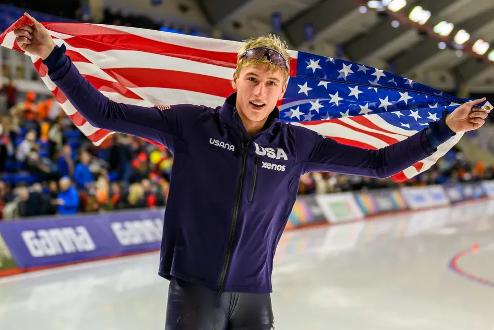 American speed skater Jordan Stolz. Wins his race and holds up the American flag. Multiple world record holder. 